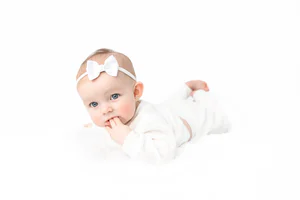 Baby girl in white outfit and bow photographed during a first-year milestone session
